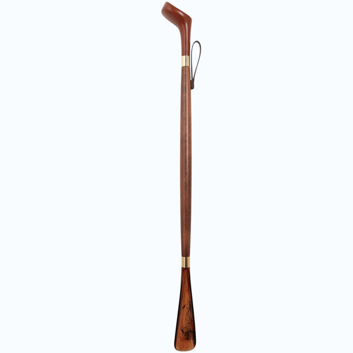 The HARVY CANES - GOLF DRIVER SHOE HORN by HARVY CANES is a long wooden shoehorn with a curved handle, brass accents, and a leather hanging loop, handcrafted in Spain and shown against a light gray background.