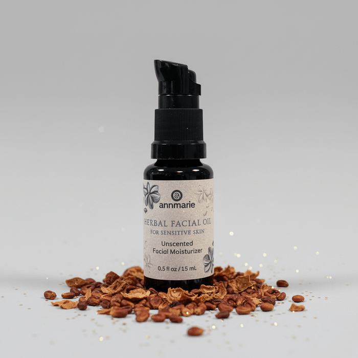 Bottle of Annmarie Herbal Facial Oil with dried herbs on a gray background