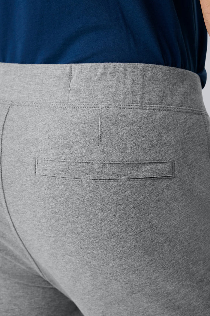 Close-up of a person wearing MACK WELDON Ace Sweatpants in True Navy Bird’s Eye with a tailored fit, drawstring waist, and pockets—one hand in the front pocket—paired with a dark blue shirt.