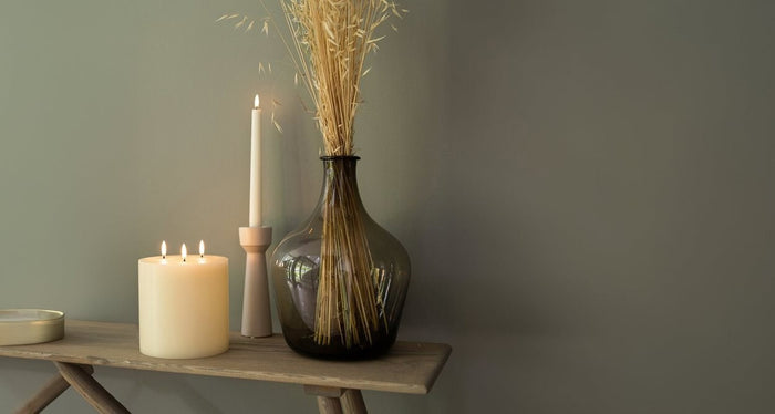 The PIFFANY UYUNI - IVORY TRIPLE FLAME PILLAR CANDLE 6X5.9 features three lit wicks that burn evenly at the top center of the large, ivory-colored candle, set against a plain white background.