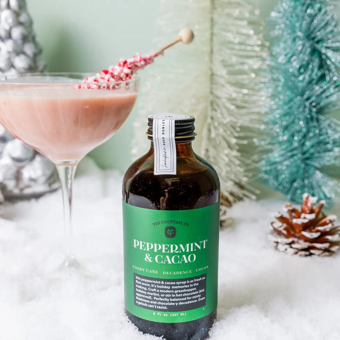 An 8 fl oz brown glass bottle from YES COCKTAIL CO. with a black cap, featuring a green label that reads “PEPPERMINT & CACAO” in white text. The YES COCKTAIL CO. PEPPERMINT & CACAO COCKTAIL SYRUP is an all-natural mixer blending candy cane freshness with decadent cocoa for a festive flavor experience.