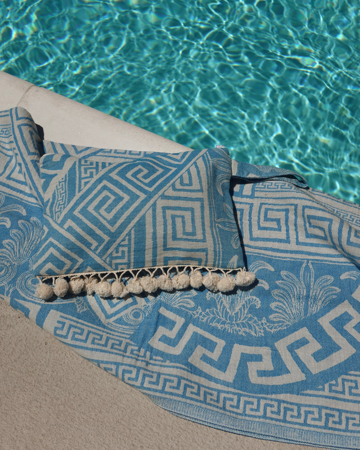Blue and cream Greek key meander print cotton towel next to a pool, pestemal towel pareo made in Greece with a matching blue Meander Greek key wet/dry clutch zippered pouch bag