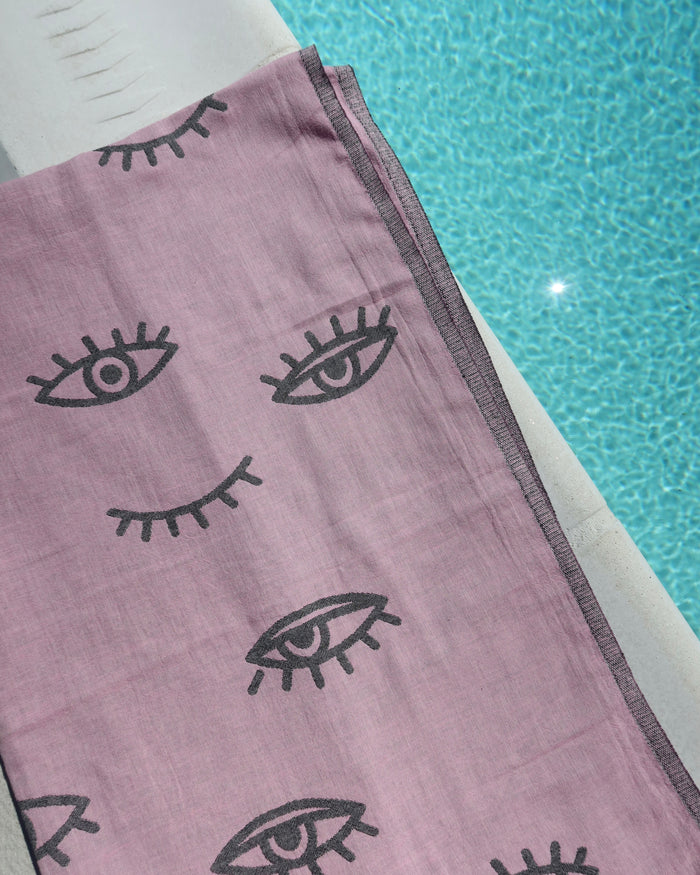 Pink towel with dark gray evil eye designs on a poolside background