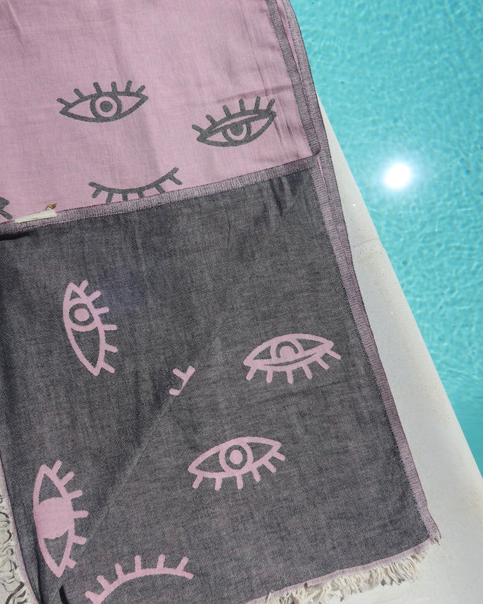 Reversible ink towel with dark gray evil eye designs on a poolside background