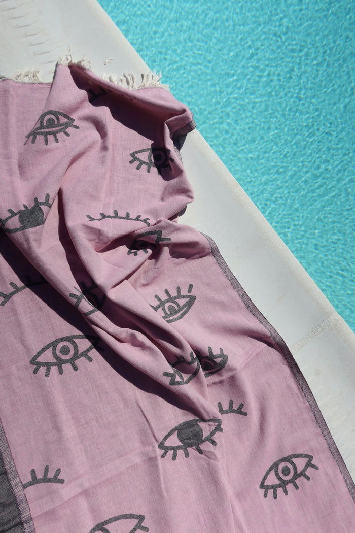 Pink towel with dark gray evil eye designs on a poolside background