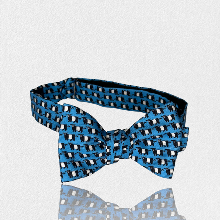 The FEARRINGTON SIGNATURE COLLECTION - BESPOKE BELTIE BOW TIE IN BLUE by COLLARED GREENS features a repeating penguin pattern on silk, set against a white textured background—an ideal men’s gift.