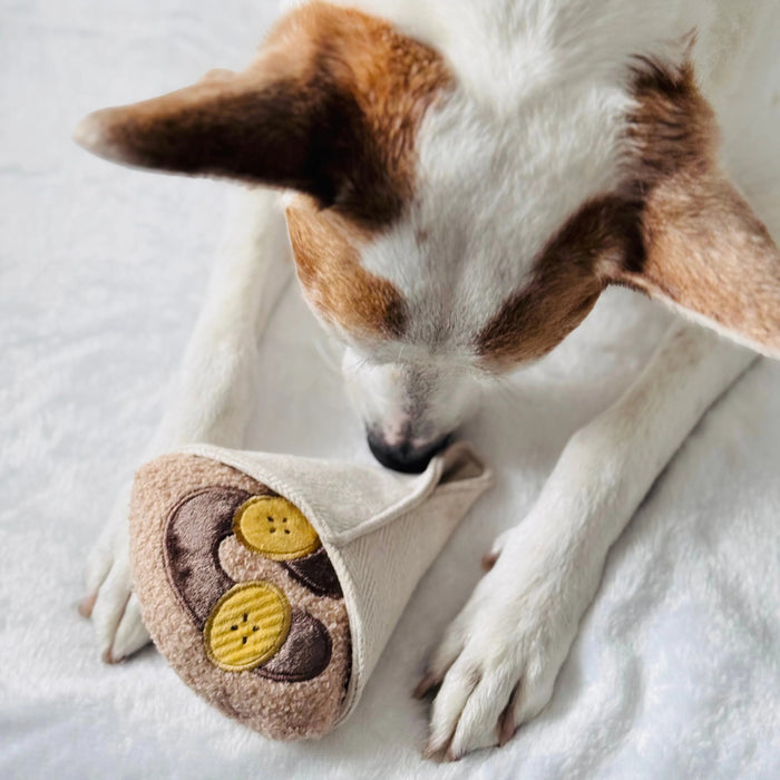 Introduce your pup to playful treat-hiding fun with the LAMBWOLF COLLECTIVE - CREPE DOG TOY by LAMBWOLF COLLECTIVE, a plush, squeaky crepe dog toy featuring brown and yellow circles that look like banana slices and chocolate sauce, all wrapped in a textured white fabric cone.