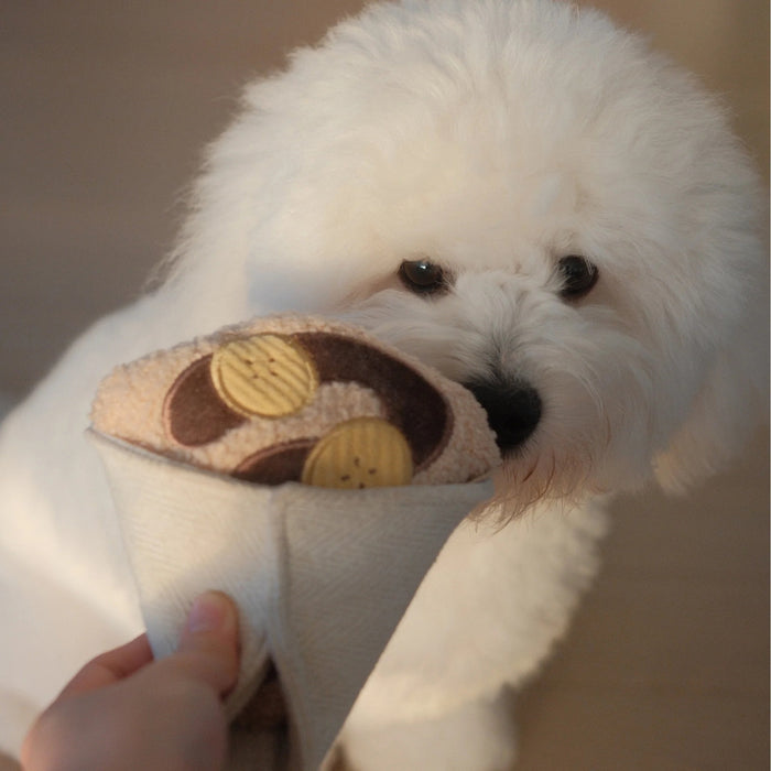 Introduce your pup to playful treat-hiding fun with the LAMBWOLF COLLECTIVE - CREPE DOG TOY by LAMBWOLF COLLECTIVE, a plush, squeaky crepe dog toy featuring brown and yellow circles that look like banana slices and chocolate sauce, all wrapped in a textured white fabric cone.