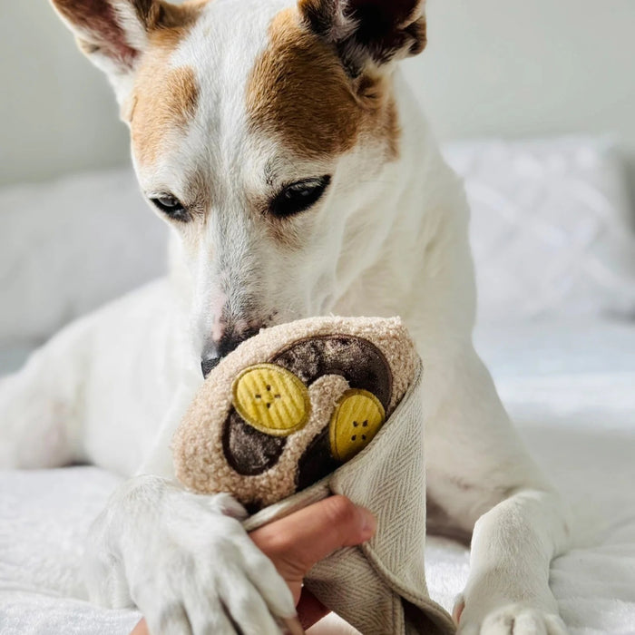 Introduce your pup to playful treat-hiding fun with the LAMBWOLF COLLECTIVE - CREPE DOG TOY by LAMBWOLF COLLECTIVE, a plush, squeaky crepe dog toy featuring brown and yellow circles that look like banana slices and chocolate sauce, all wrapped in a textured white fabric cone.