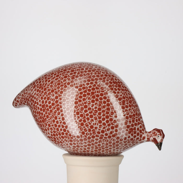 A round, handmade ceramic guinea hen sculpture from LES CERAMIQUES DE LUSSAN—the PECKING CERAMIC FRENCH GUINEA IN BORDEAUX SPOTTED WHITE—stands on a white pedestal against a plain background, showcasing French artistry in pottery and the brand’s iconic spotted pattern.