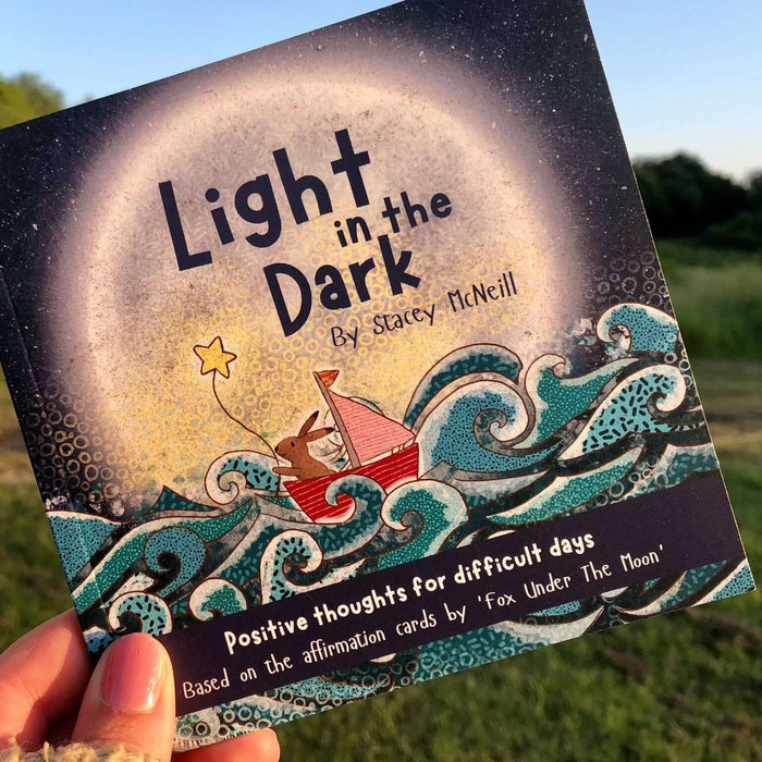 Book titled 'Light in the Dark' held in a hand with a natural background