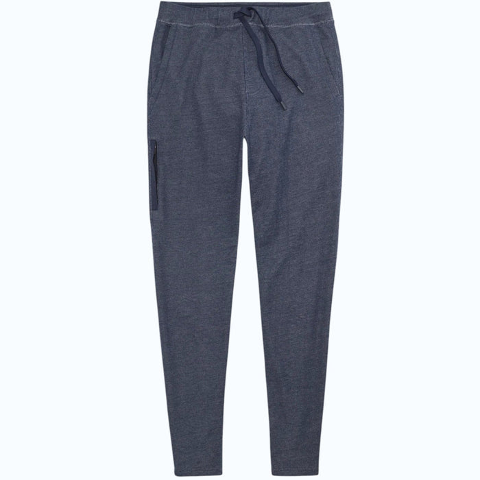 Close-up of a person wearing MACK WELDON Ace Sweatpants in True Navy Bird’s Eye with a tailored fit, drawstring waist, and pockets—one hand in the front pocket—paired with a dark blue shirt.