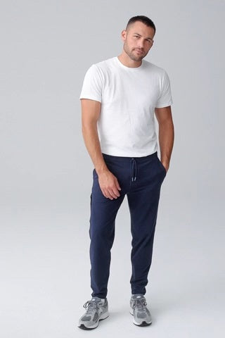 Close-up of a person wearing MACK WELDON Ace Sweatpants in True Navy Bird’s Eye with a tailored fit, drawstring waist, and pockets—one hand in the front pocket—paired with a dark blue shirt.