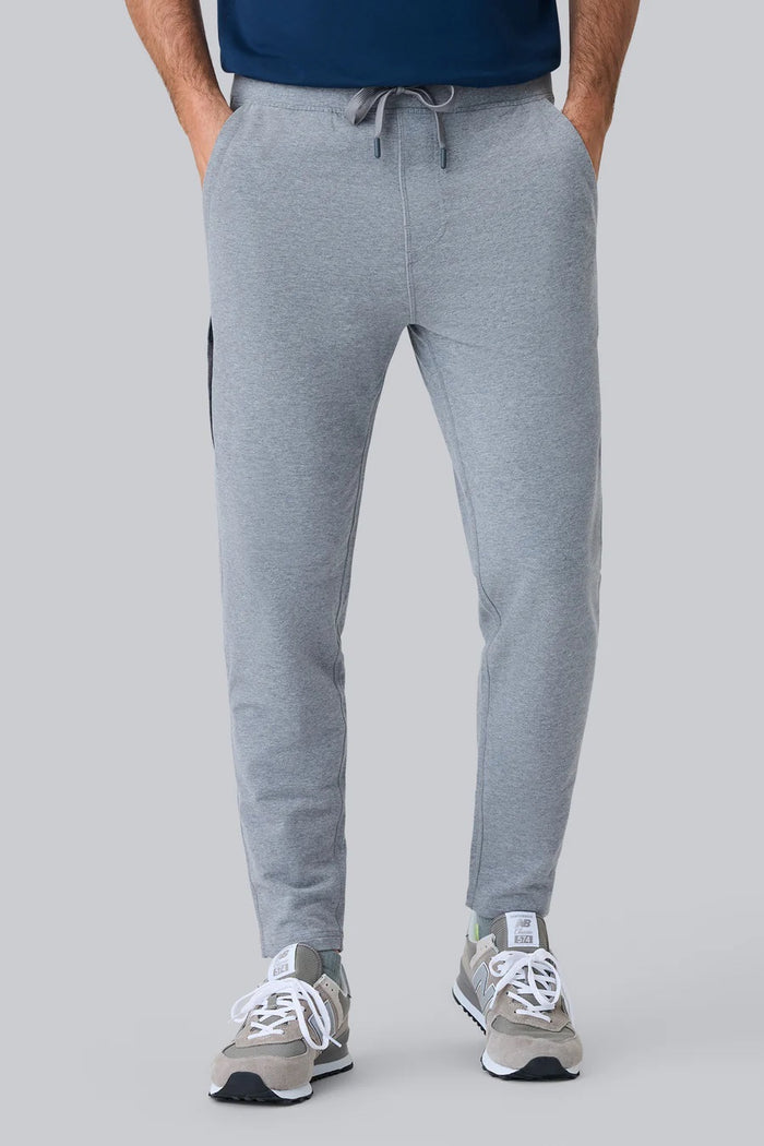 Close-up of a person wearing MACK WELDON Ace Sweatpants in True Navy Bird’s Eye with a tailored fit, drawstring waist, and pockets—one hand in the front pocket—paired with a dark blue shirt.
