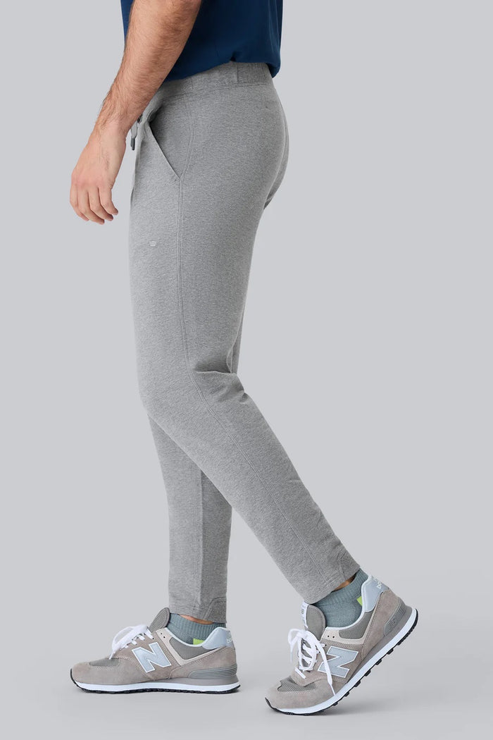 Close-up of a person wearing MACK WELDON Ace Sweatpants in True Navy Bird’s Eye with a tailored fit, drawstring waist, and pockets—one hand in the front pocket—paired with a dark blue shirt.