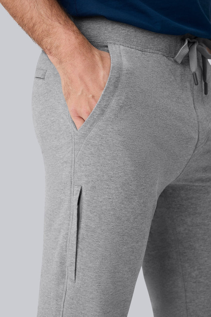 Close-up of a person wearing MACK WELDON Ace Sweatpants in True Navy Bird’s Eye with a tailored fit, drawstring waist, and pockets—one hand in the front pocket—paired with a dark blue shirt.