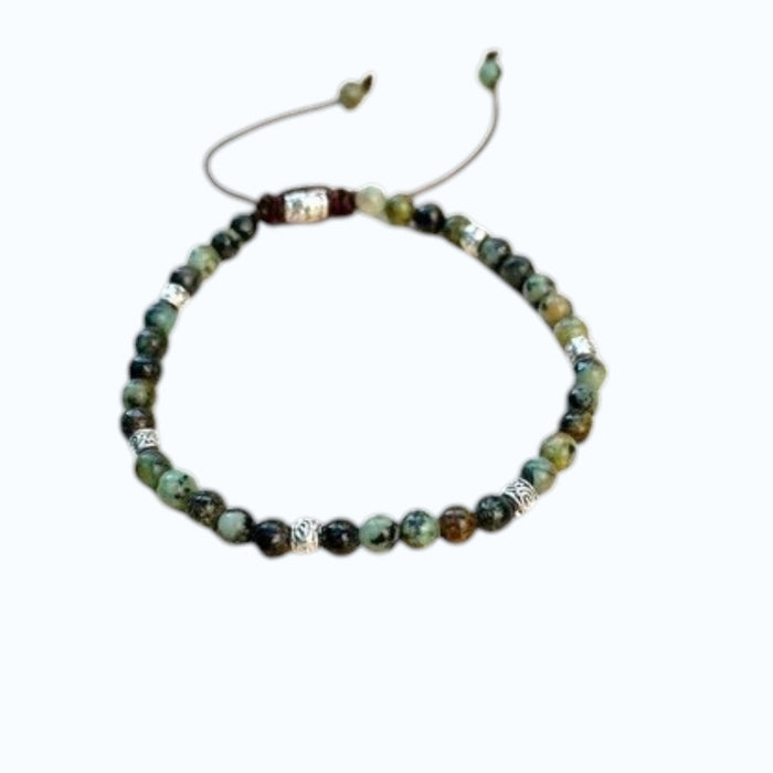 The STOLEN RICHES Formentera Bracelet in African Turquoise Stone features green and brown beads with silver accents on an adjustable brown cord, adding earthy elegance to any style.