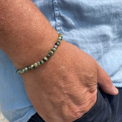 The STOLEN RICHES Formentera Bracelet in African Turquoise Stone features green and brown beads with silver accents on an adjustable brown cord, adding earthy elegance to any style.