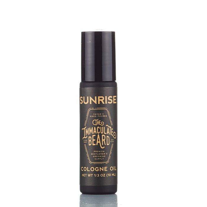 THE IMMACULATE BEARD - COLOGNE OIL IN SUNRISE is a premium 10ml beard cologne oil with a woody scent, sleek black bottle, gold text, and convenient rollerball applicator from THE IMMACULATE BEARD.