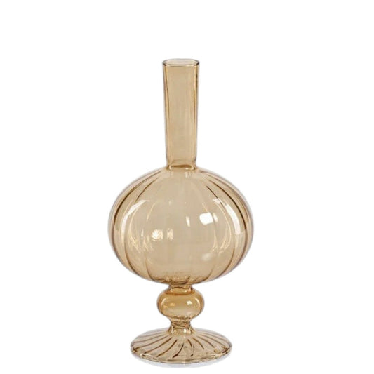 Five amber glass vases of varying heights and shapes, including the striking ZODAX VENETIAN SPIRAL VASE IN AMBER ONION SHAPE (7.5”), are arranged together on a textured surface. Some contain delicate, decorative branches with small beads, set against a softly lit, neutral-toned background.